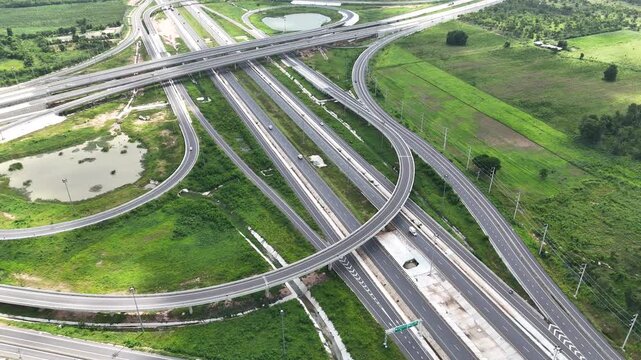 Aerial view of modern highway interchange with multilayer roads and curved ramps surrounded by green farmland, showcasing transportation infrastructure, urban development, and road network planning.