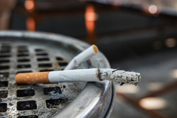 Cigarette butts in metal ashtray with smoke and ash. Burning cigarette butts in ashtray, Smoking concept close-up. © All times 