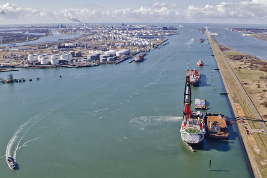 Hoek van Holland, Netherlands - 15 February 2026: Aerial view of ships navigating the waterway towards an industrial landscape, where tanks gleam under the soft winter light.
