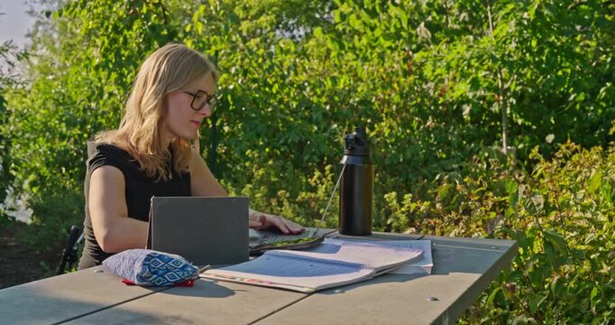 A young white college student studying outdoors for their exams on a nice sunny day.