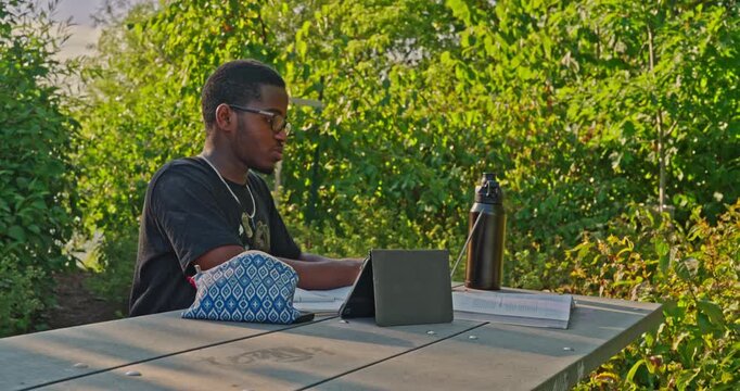 Young black male reviewing class notes on a sunny day in a public park.