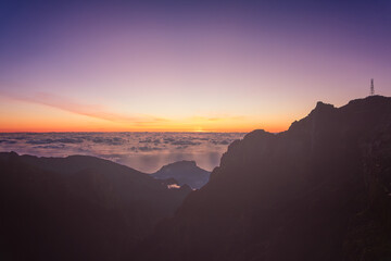 Sunrise panorama from Miradouro do Pico do Areiro Madeira Portugal, film style travel mood with pastel sky sea of clouds and mountain silhouettes slowly warmed by early light