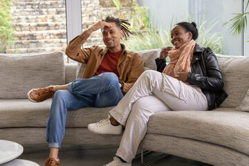 Obraz premium African American couple sitting on light gray sectional sofa in bright living room, holding scarf