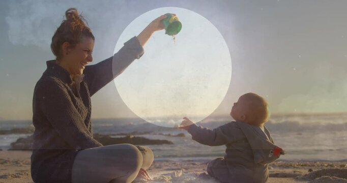 Mother tilting green cup and pouring sand to baby, overlay growing around sand, showing family bond