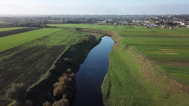 Scenic drone shot capturing the main course of the Loukkos river. Features the river's natural curve, high embankments, and the expansive fertile farmlands characteristic of Northern Morocco.
