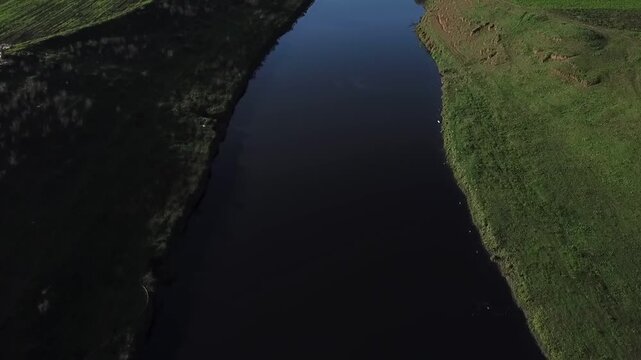 Top-down drone shot focusing on the expansive water surface of the Loukkos river. Highlights the deep blue currents and the vibrant green banks of Morocco's most vital northern waterway.