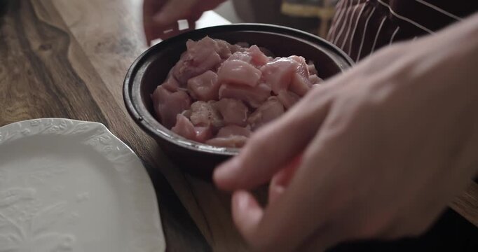 Chef moving cutting board to show ceramic bowl filled with chopped raw chicken breast meat on wooden table, preparing healthy protein ingredients for home cooked meal in cozy kitchen