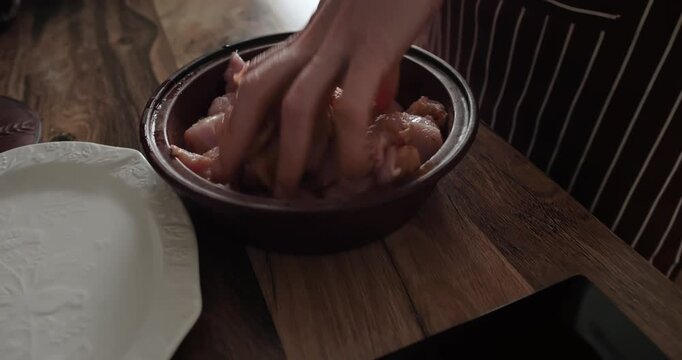 Chef seasoning and mixing raw chopped chicken breast fillet with spices in ceramic bowl on wooden table, preparing healthy protein meal in cozy home kitchen. Healthy food, diet