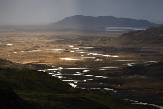 View of a winding river snaking through a vast, sun-kissed landscape under a moody sky, with distant mountains adding depth and drama, Reykjav&Atilde;&shy;k, Iceland.