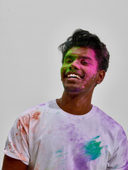 Fototapeta premium Young man smiling with colorful powder stains on face and shirt. Concept of festive spring event, casual youth fashion style, cultural celebration atmosphere and lifestyle branding content.