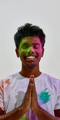Fototapeta premium Smiling man with hands in namaste covered in colored powder. Concept of Holi greeting ritual, cultural diversity message, respectful celebration scene and bright lifestyle campaign visual.