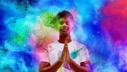 Fototapeta premium Young man praying during Holi festival with colorful powder explosion. Concept of spiritual celebration, cultural heritage, mindful moment and vibrant creative background for festival campaigns.