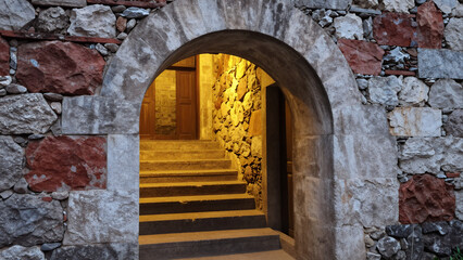 Fototapeta premium Stone Archway Entrance With Warm-Lit Staircase Leading To Inner Corridor Of Medieval Building