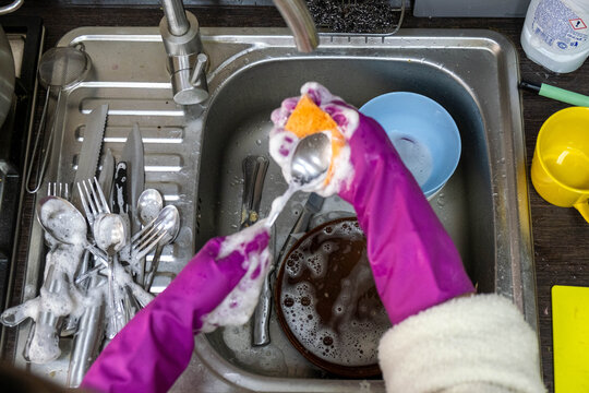 Washing dishes in kitchen sink with purple rubber gloves Copy Space