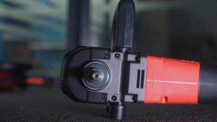 Detailed close up of a red and black electric angle grinder placed on a dark surface, showcasing the tool's mechanism.