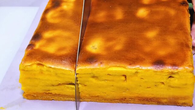 A close-up of hands using a knife to slice Lapis Legit, a thousand-layer cake.