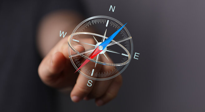 Hand reaching out to a digital compass pointing North, South, East, West. Represents direction, guidance, and navigation