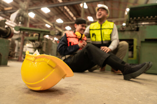 A yellow safety helmet lies on the floor as workers in the background react to an accident, emphasizing the importance of always wearing protective gear in hazardous environments.