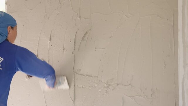 Female construction worker applying cement plaster with trowel on interior wall. Skilled labor, building renovation and equality in construction industry concept.