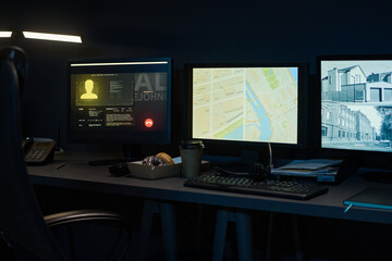 Naklejka premium Three computer monitors displaying digital map, surveillance footage, and user profile on dark desk with keyboard, telephone, takeaway coffee cup and pastry box in modern workspace