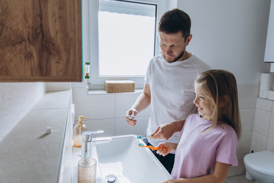 Father and daughter brushing teeth together in bathroom morning