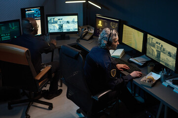 Middle aged Caucasian woman and Black man monitoring multiple surveillance screens in security...