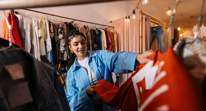 Customer Selects Coat. Shoppers Are Immersed In Browsing And Feeling Different Styles Of Clothing Items