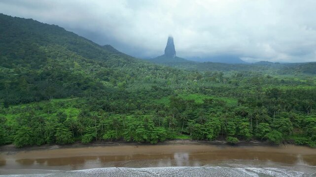 Flying sideways over the sea from Praia Grande, with the waves crashing with the majestic Pico Cao Grande and the green forest at background.S&atilde;o Tom&eacute;,Africa