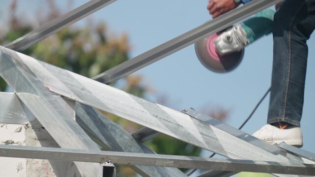 Construction technician drilling steel beam on roof structure against blue sky. Industrial metal framework, engineering precision and high level construction concept.