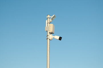 A CCTV camera and a spotlight on a pole against a blue sky