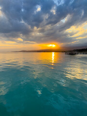 Fototapeta premium Turquoise water of Issyk Kul at sunset with golden reflection and dramatic clouds.