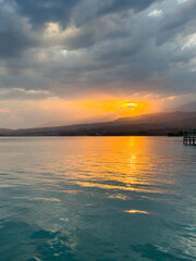 Obraz premium Scenic sunset over Issyk Kul Lake in Kyrgyzstan. The sun sets behind the mountains, casting a golden reflection across the water.