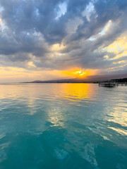 Fototapeta premium Sunset at Issyk Kul Lake in Kyrgyzstan. Bright sun breaking through clouds reflecting in clear turquoise water.