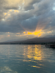 Fototapeta premium Turquoise water of Issyk Kul at sunset with golden reflection and dramatic clouds.