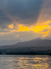 Fototapeta premium Sunset at Issyk Kul Lake in Kyrgyzstan. Bright sun breaking through clouds reflecting in clear turquoise water.