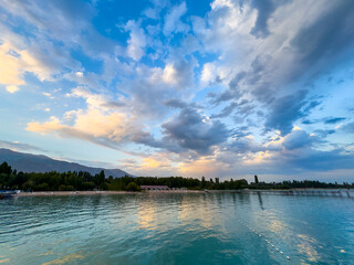 Obraz premium Issyk Kul Lake in Kyrgyzstan. Calm turquoise water reflecting clouds with soft evening light over beach and pier.