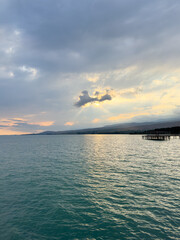 Fototapeta premium Sunset at Issyk Kul Lake in Kyrgyzstan. Bright sun breaking through clouds reflecting in clear turquoise water.