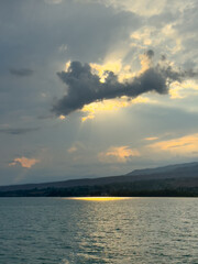 Fototapeta premium Sunset at Issyk Kul Lake in Kyrgyzstan. Bright sun breaking through clouds reflecting in clear turquoise water.