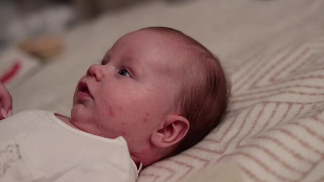 Close-up profile of a newborn baby with rosy cheeks and soft hair lying on a patterned blanket