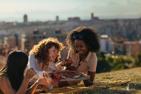 Friends sharing pizza at a sunset picnic on a rooftop hill with Madrid city skyline in the background