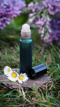 Vertical video of natural eye serum or perfume roll-on bottle on grass with blooming lilac. Botanical DIY cosmetics concept, organic beauty product in spring garden atmosphere.