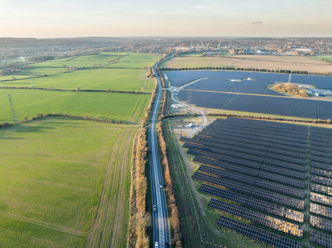 Aerial view of solar panels reflecting the sky's soft glow beside verdant fields and a winding road, Cowley, Oxfordshire, United Kingdom.