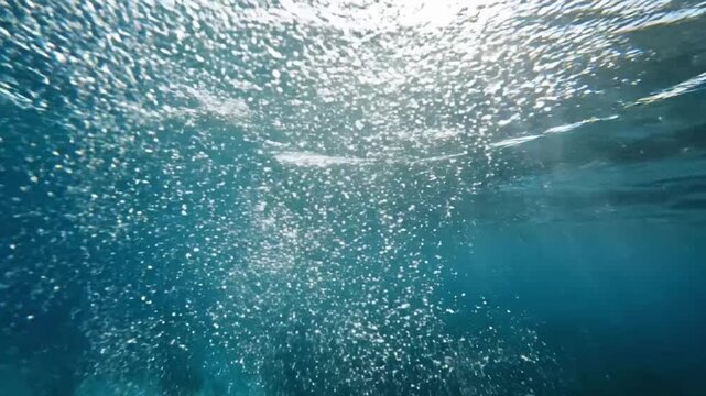 Bubbles rise in clear water over coral reef with sunlight shining through surface at midday
