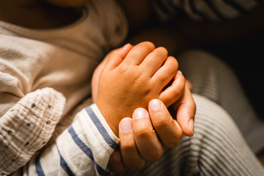 Close up of mother holding hands of hispanic baby toddler with sof light. Concept of real motherhood and bond. Care, love, relationship concept.