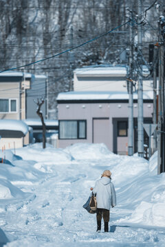 View of a solitary figure walks along a snowy path lined with houses, the snow-covered landscape creating a serene and cold ambiance, Biei, Hokkaido, Japan.