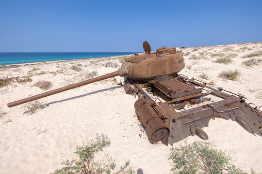 View of a weathered, decaying tank, its rusted metal stark against the pristine white sand and the vibrant turquoise ocean, Qalansiyah, Socotra, Yemen.