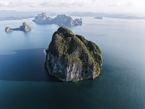 Aerial view of a rugged, verdant island rising majestically from the tranquil, turquoise waters, framed by distant, hazy landforms, Palawan, Philippines.