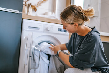 Woman sorting clean towels by washing machine, laundry day in modern bathroom, home cleaning routine and sunday reset concept, housekeeping and hygiene lifestyle, cozy neutral interior.