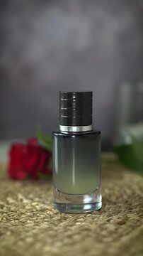 Close-up vertical video of black perfume bottle with cap and red rose on dark and beige background. Elegant fragrance concept combining luxury perfume and natural homemade essential oil scent.