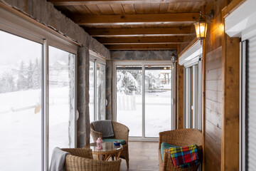 Warm Mountain Lodge Interior with Wicker Chair, Coffee Table, and Snowy Winter Terrace View.